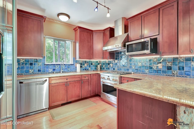 7408 N Grouse Loop, Wasilla, AK 99654 - kitchen featuring appliances with stainless steel finishes, wall chimney exhaust hood, light wood-style floors, light stone countertops, and backsplash