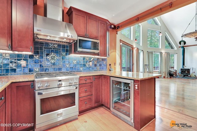 7408 N Grouse Loop, Wasilla, AK 99654 - kitchen with stainless steel appliances, beverage cooler, wall chimney range hood, a wood stove, and light wood-style floors