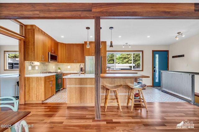 1601 Bannister Dr, Anchorage, AK 99508 - kitchen featuring stainless steel appliances, light countertops, tasteful backsplash, brown cabinetry, and a kitchen island with sink