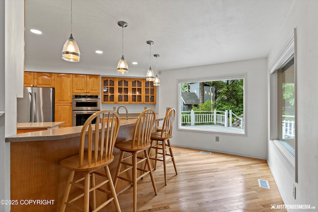 1701 Woo Blvd, Anchorage, AK 99515 - kitchen with stainless steel appliances, glass insert cabinets, light wood-type flooring, brown cabinets, and a kitchen bar