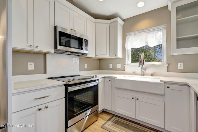 5893 Kenai Fjords Loop, Anchorage, AK 99502 - kitchen featuring appliances with stainless steel finishes, a sink, white cabinetry, glass insert cabinets, and light wood-type flooring