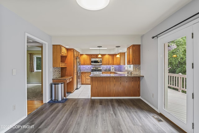 11751 Mary Ave, Anchorage, AK 99515 - kitchen featuring stainless steel appliances, brown cabinets, a peninsula, light wood-style floors, and tasteful backsplash