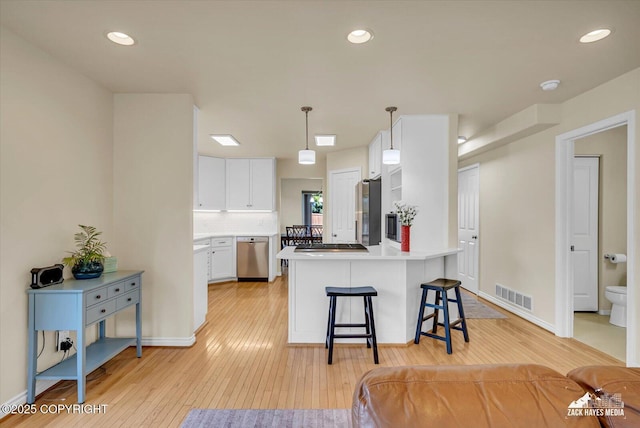 10201 Sextant Cir, Anchorage, AK 99515 - kitchen featuring white cabinets, light wood-style floors, appliances with stainless steel finishes, a breakfast bar, and light countertops