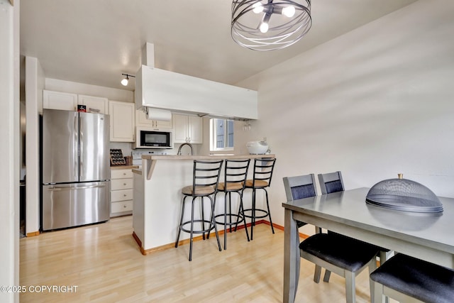 4160 Crannog St, Anchorage, AK 99502 - kitchen featuring freestanding refrigerator, a peninsula, white cabinets, a breakfast bar area, and light wood-style flooring
