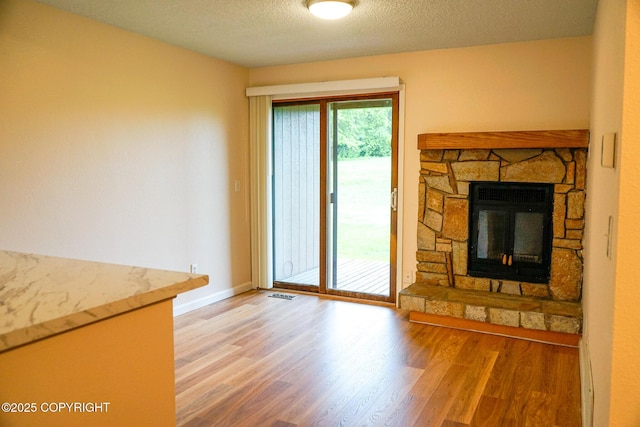 2100 Minerva Way # A6, Anchorage, AK 99515 - unfurnished living room with wood finished floors, baseboards, a stone fireplace, and a textured ceiling