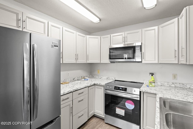 1100 Fred Cir, Anchorage, AK 99515 - kitchen with stainless steel appliances, light wood finished floors, a textured ceiling, light stone counters, and white cabinetry