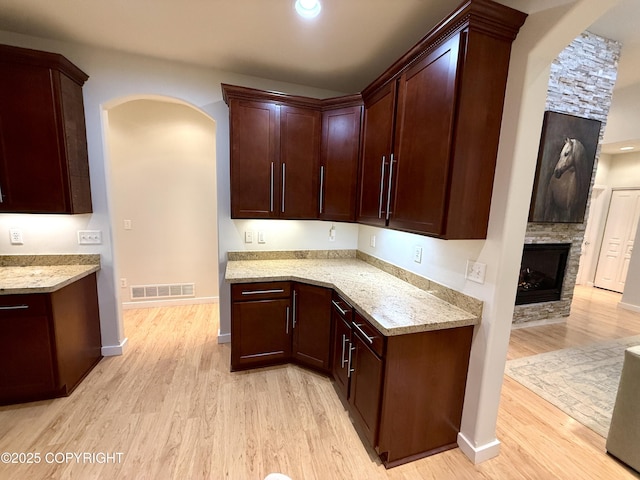 14740 Maxwell Pl, Anchorage, AK 99516 - kitchen with arched walkways, light wood finished floors, light stone countertops, baseboards, and a stone fireplace