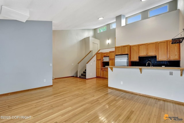 3135 Delta Dr, Anchorage, AK 99502 - kitchen featuring stainless steel refrigerator, a kitchen bar, white microwave, a peninsula, and light wood-style floors