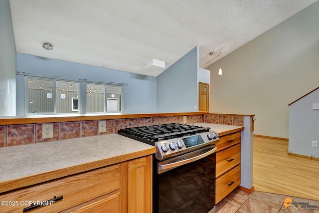 3135 Delta Dr, Anchorage, AK 99502 - kitchen featuring stainless steel range with gas stovetop, decorative backsplash, light countertops, vaulted ceiling, and light tile patterned floors