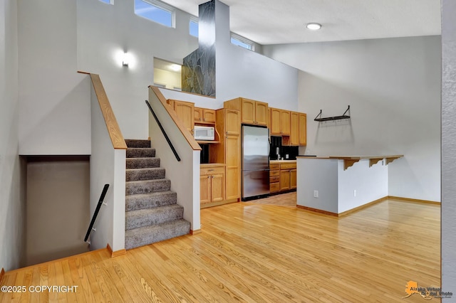 3135 Delta Dr, Anchorage, AK 99502 - kitchen featuring freestanding refrigerator, a towering ceiling, light wood-style floors, white microwave, and a peninsula