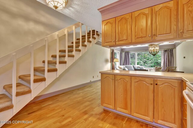 836 O Pl, Anchorage, AK 99501 - kitchen with light wood-style flooring, a textured ceiling, a chandelier, light countertops, and a peninsula
