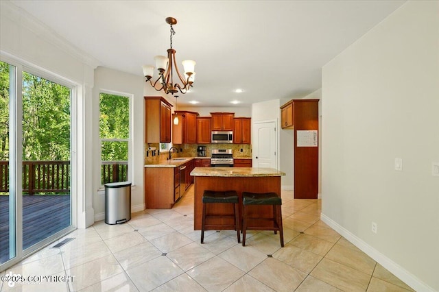 4920 W Fairview Loop, Wasilla, AK 99654 - kitchen with stainless steel appliances, a chandelier, brown cabinetry, a kitchen island, and tasteful backsplash