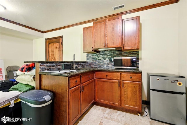 4920 W Fairview Loop, Wasilla, AK 99654 - kitchen with appliances with stainless steel finishes, decorative backsplash, a peninsula, brown cabinetry, and ornamental molding