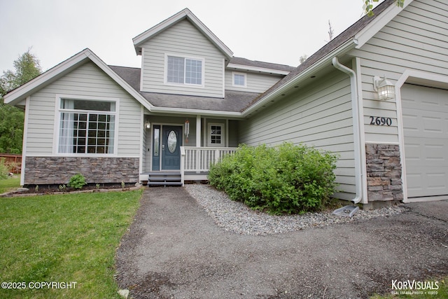 2690 E Tamarak Ave, Wasilla, AK 99654 - view of front of home featuring covered porch, stone siding, an attached garage, roof with shingles, and a front lawn