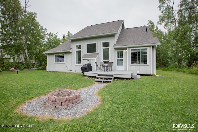 2690 E Tamarak Ave, Wasilla, AK 99654 - rear view of house featuring an outdoor fire pit, a wooden deck, roof with shingles, and a lawn