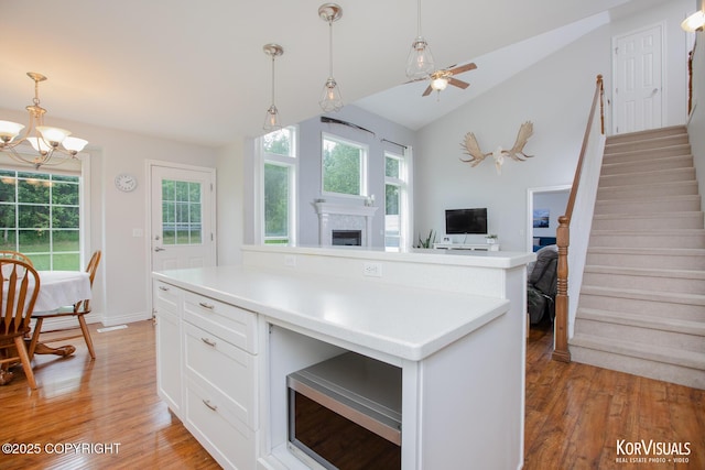 2690 E Tamarak Ave, Wasilla, AK 99654 - kitchen featuring light wood-type flooring, a fireplace, a chandelier, white cabinetry, and vaulted ceiling
