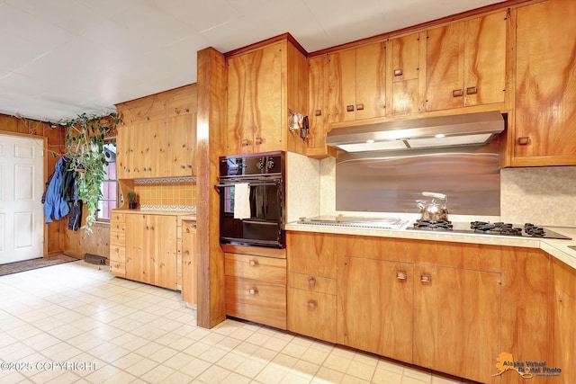 3200 E 15th Ave, Anchorage, AK 99508 - kitchen featuring under cabinet range hood, black oven, decorative backsplash, light countertops, and brown cabinetry