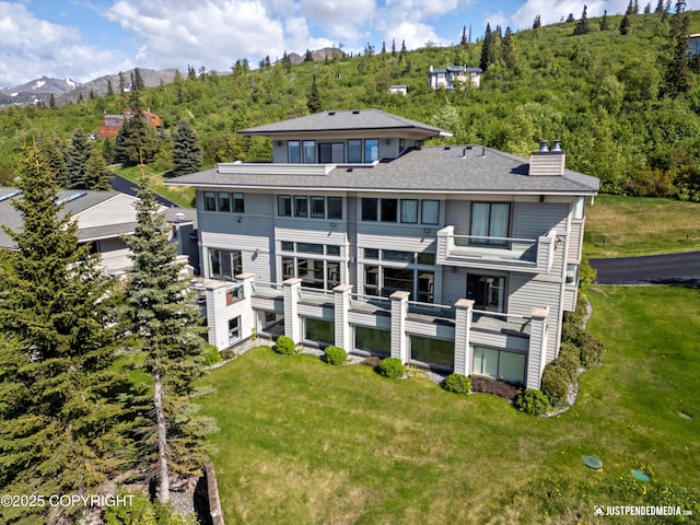 9900 Hillhaven Cir, Anchorage, AK 99507 - rear view of property with a balcony, a chimney, a forest view, a mountain view, and a lawn