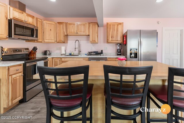 799 8th Ave, Fairbanks, AK 99701 - kitchen with stainless steel appliances, a sink, light brown cabinets, light wood-style flooring, and a breakfast bar