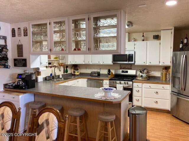 50470 Maranatha Ln, Nikiski/North Kenai, AK 99611 - kitchen featuring appliances with stainless steel finishes, a peninsula, white cabinets, glass insert cabinets, and a kitchen bar