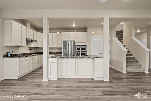 2987 Morgan Loop, Anchorage, AK 99516 - kitchen with stainless steel appliances, white cabinetry, dark stone countertops, light wood-style flooring, and a kitchen island with sink