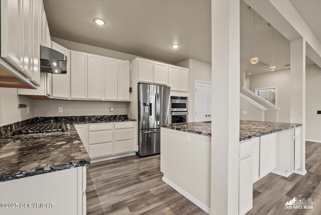 2987 Morgan Loop, Anchorage, AK 99516 - kitchen with appliances with stainless steel finishes, ventilation hood, wood finished floors, dark stone counters, and white cabinetry