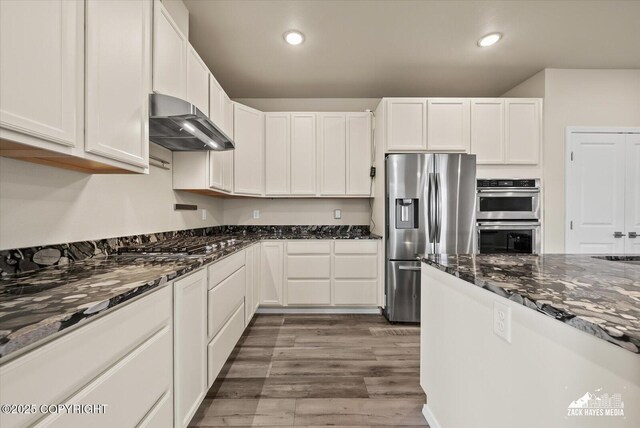 2987 Morgan Loop, Anchorage, AK 99516 - kitchen with stainless steel appliances, wall chimney range hood, white cabinetry, dark stone countertops, and wood finished floors