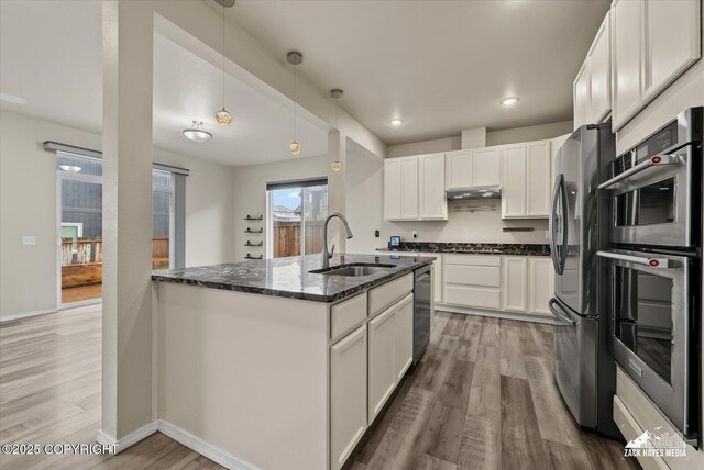2987 Morgan Loop, Anchorage, AK 99516 - kitchen with stainless steel appliances, dark stone counters, light wood-type flooring, white cabinetry, and decorative light fixtures