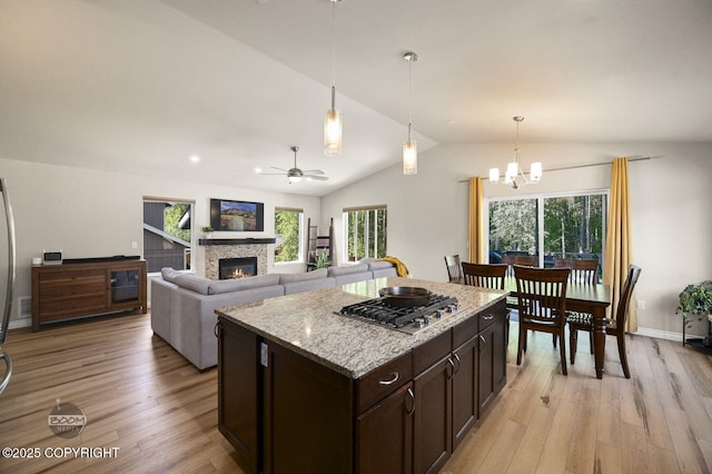 13378 Rosser Dr, Eagle River, AK 99577 - kitchen featuring stainless steel gas cooktop, vaulted ceiling, dark brown cabinetry, light wood-style floors, and a glass covered fireplace
