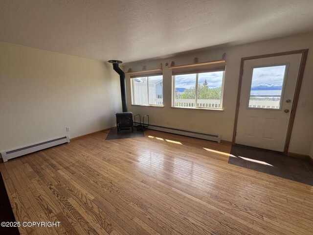 705 W Fairview Ave, Homer, AK 99603 - unfurnished living room with a baseboard radiator, a wood stove, wood-type flooring, and a textured ceiling