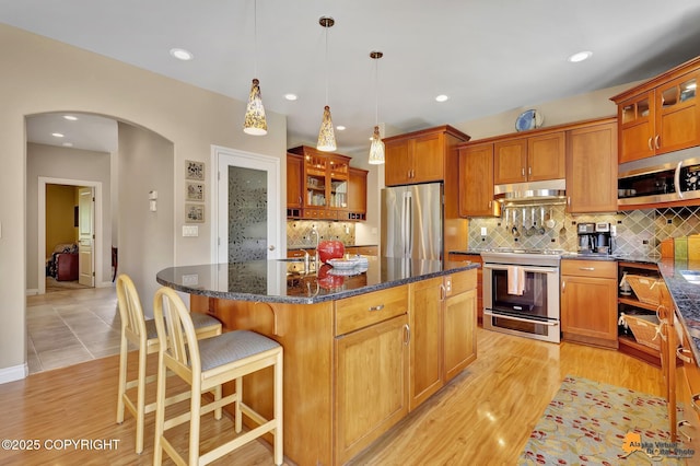2842 Ensign Dr, Anchorage, AK 99515 - kitchen with appliances with stainless steel finishes, under cabinet range hood, arched walkways, a center island, and brown cabinets