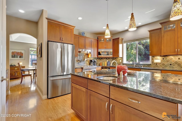 2842 Ensign Dr, Anchorage, AK 99515 - kitchen featuring appliances with stainless steel finishes, brown cabinetry, light wood finished floors, arched walkways, and dark stone countertops