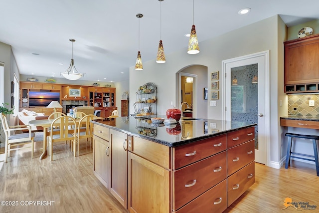 2842 Ensign Dr, Anchorage, AK 99515 - kitchen featuring tasteful backsplash, light wood-style floors, arched walkways, pendant lighting, and a center island with sink