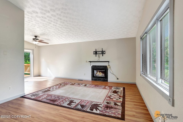 3091 N Longspur Dr, Wasilla, AK 99654 - unfurnished living room with a textured ceiling, wood finished floors, a glass covered fireplace, and a ceiling fan