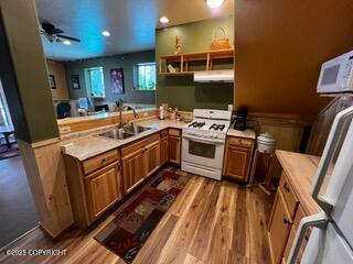 18905 Langille Rd, Cooper Landing, AK 99572 - kitchen featuring white gas range, brown cabinets, a wainscoted wall, exhaust hood, and light countertops