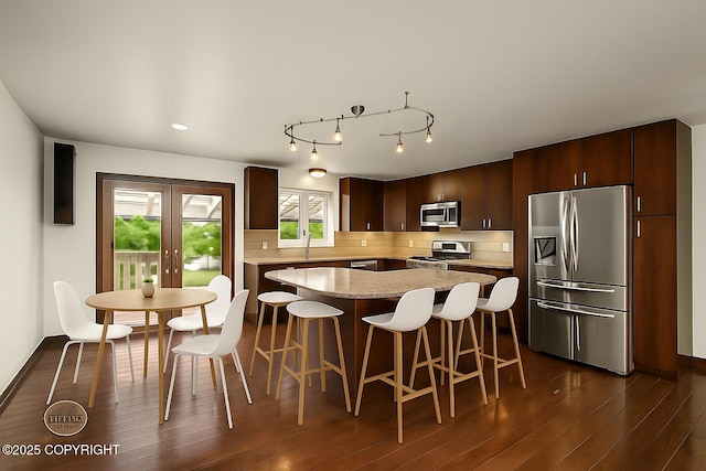10010 Colville St, Eagle River, AK 99577 - kitchen with appliances with stainless steel finishes, dark wood-style floors, dark brown cabinetry, decorative backsplash, and a breakfast bar area