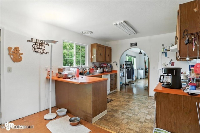 701 N Luke St, Wasilla, AK 99654 - kitchen featuring arched walkways, brown cabinetry, white dishwasher, a peninsula, and light countertops