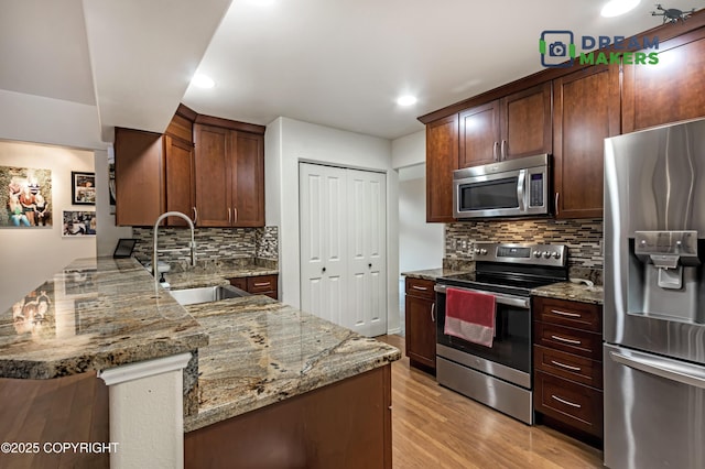11240 E Equestrian St, Palmer, AK 99645 - kitchen featuring appliances with stainless steel finishes, a peninsula, decorative backsplash, light stone countertops, and light wood-type flooring