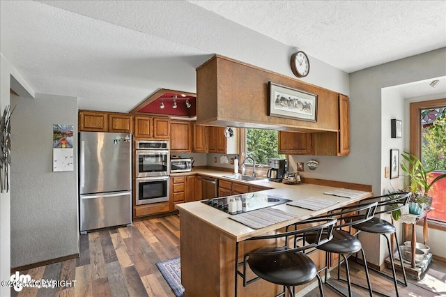 19360 Chugach Park Dr, Chugiak, AK 99567 - kitchen featuring stainless steel appliances, brown cabinetry, a peninsula, dark wood finished floors, and light countertops