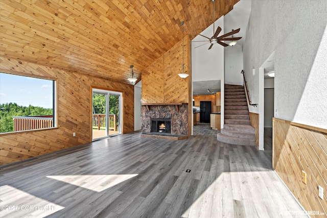 19712 Chugach Park Dr, Eagle River, AK 99567 - unfurnished living room featuring high vaulted ceiling, a fireplace, stairway, wood walls, and a ceiling fan