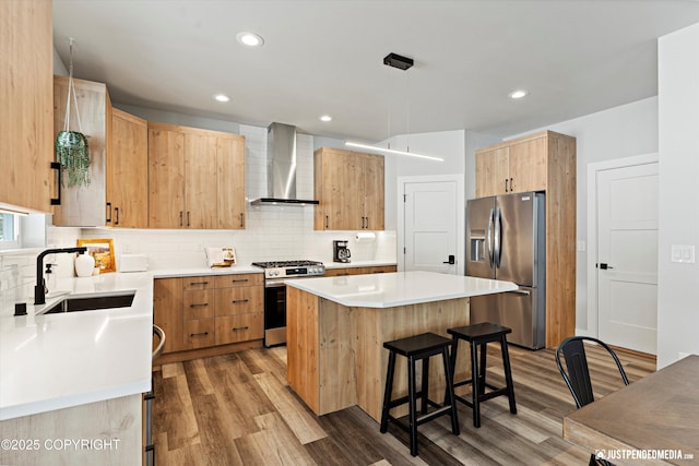 9203 Strutz Ave, Anchorage, AK 99507 - kitchen with wall chimney range hood, appliances with stainless steel finishes, a center island, a kitchen bar, and light wood-type flooring