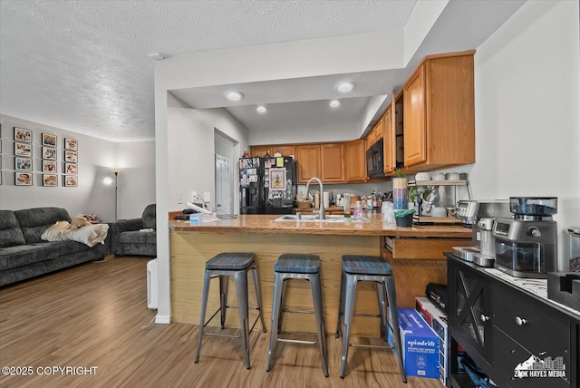 5320 Larkspur St, Anchorage, AK 99507 - kitchen with black appliances, light wood-style flooring, brown cabinetry, a breakfast bar, and a textured ceiling