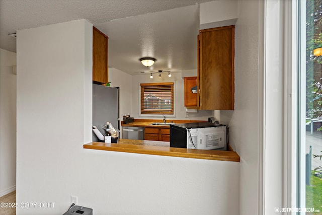 10201 Jamestown Dr # A102, Anchorage, AK 99507 - kitchen featuring stainless steel appliances, brown cabinets, a textured ceiling, and rail lighting