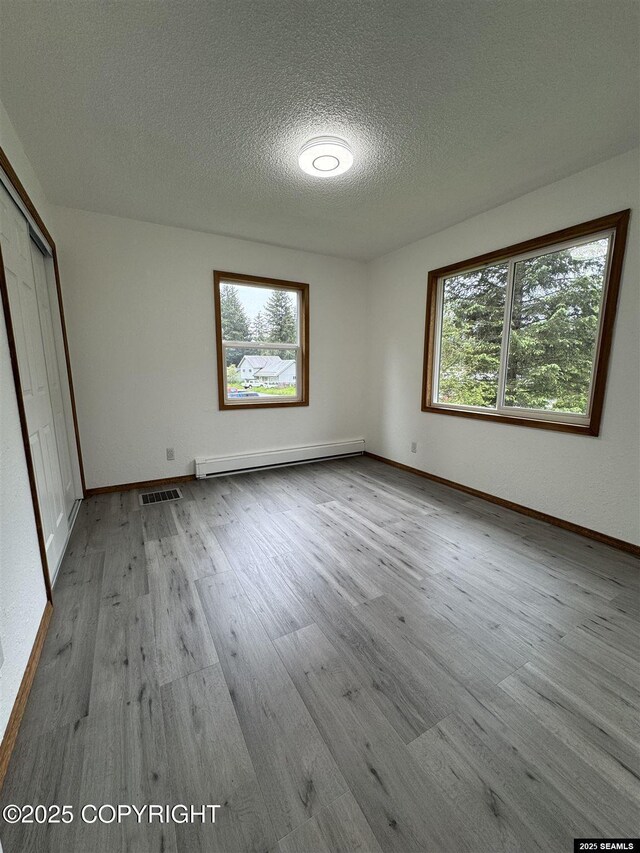5920 Lund St, Juneau, AK 99801 - unfurnished bedroom with a baseboard heating unit, wood finished floors, multiple windows, a textured ceiling, and a closet