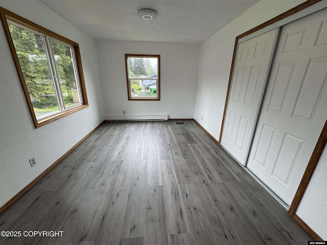 5920 Lund St, Juneau, AK 99801 - unfurnished bedroom featuring a baseboard heating unit, wood finished floors, a textured ceiling, and a closet