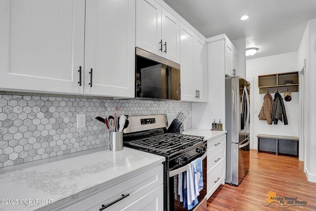 4576 S Gon Fishin Dr, Wasilla, AK 99623 - kitchen featuring appliances with stainless steel finishes, light wood finished floors, white cabinetry, decorative backsplash, and light stone counters