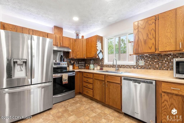 17311 Bonasila Cir, Eagle River, AK 99577 - kitchen with stainless steel appliances, brown cabinetry, light countertops, a textured ceiling, and backsplash
