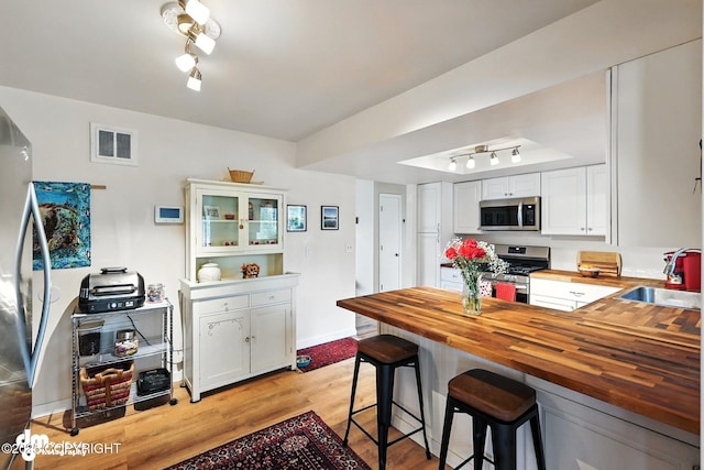 222 Crest Dr, Soldotna, AK 99669 - kitchen with appliances with stainless steel finishes, butcher block countertops, light wood-type flooring, white cabinetry, and track lighting