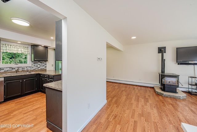 312 W Riverview Ave, Soldotna, AK 99669 - kitchen featuring a baseboard radiator, light wood finished floors, decorative backsplash, a wood stove, and light stone countertops
