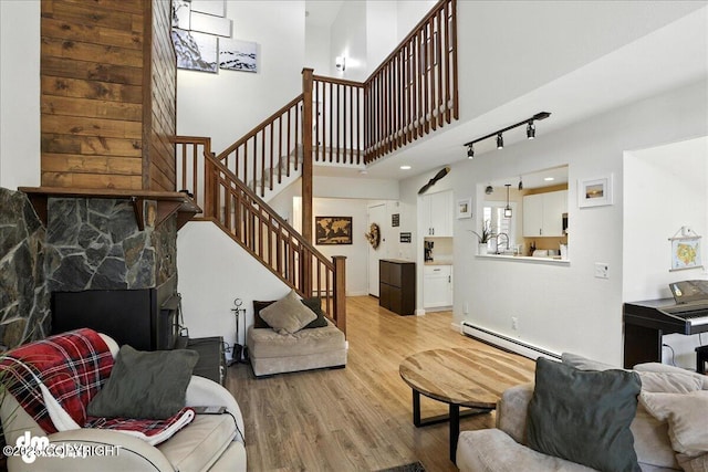 6622 Lakeway Dr, Anchorage, AK 99502 - living room featuring a baseboard heating unit, stairs, light wood-style floors, rail lighting, and a stone fireplace